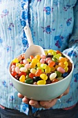 Hand holding bowl of coloured jelly beans with scoop