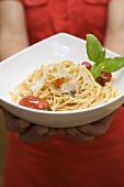 Hands holding plate of spaghetti with Parmesan and basil