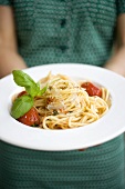 Frau hält Teller Spaghetti mit Parmesan und Basilikum