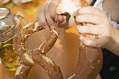 Hände brechen Stück von Laugenbrezel (München, Oktoberfest)