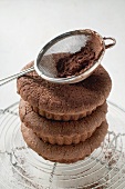 Three chocolate buns, in a pile, cocoa powder in sieve