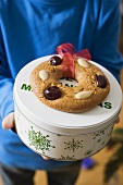 Person holding biscuit tin with gingerbread tree ornament