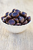 Chestnuts in white bowl on wooden background