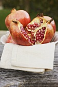 Pomegranates, whole and halved, on cloth in white bowl
