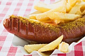 Sausage with ketchup & curry powder & chips in paper dish (close-up)