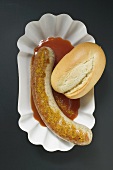 Sausage with curry powder, ketchup & bread roll (overhead view)