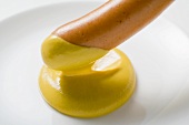 Dipping frankfurter in mustard (close-up)