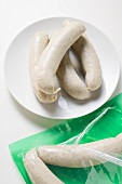 Fresh sausages on plate and in packaging