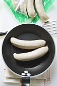 Fresh sausages in frying pan and opened packaging