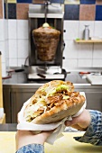 Hands holding a döner kebab in a snack bar
