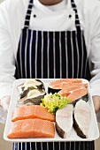 Person holding tray of salmon and sea bass pieces