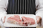 Person holding two T-bone steaks on tray