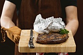 Man holding grilled beef steak on chopping board