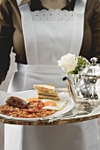 Chambermaid serving English breakfast on tray