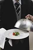Butler serving tomato and parsley on plate with dome cover