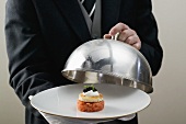 Butler serving salmon tartare on plate with domed cover