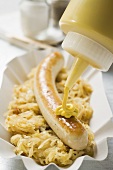 Senf auf Grillwurst mit Sauerkraut geben