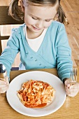 Girl sitting in front of plate of ribbon pasta & tomato sauce