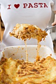 Woman taking portion of lasagne out of baking dish