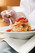 Person eating spaghetti with tomatoes and rosemary