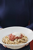 Hands holding a plate of linguine with tomato sauce