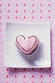 Pink heart-shaped petit four on plate (overhead view)