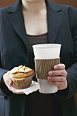 Woman holding muffin and plastic coffee cup