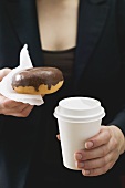 Frau hält Doughnut und Kaffeebecher