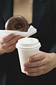 Woman holding doughnut and plastic coffee cup