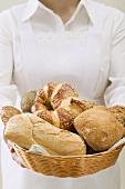 Chambermaid serving assorted bread rolls in bread basket