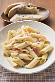 Penne with salmon and cream sauce, slices of bread behind