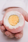 Child's hands holding coloured boiled egg with top cut off