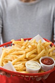 Frau hält Korb mit Pommes frites, Ketchup und Mayonnaise