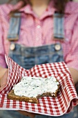Woman holding wholemeal bread with quark & ramsons on napkin