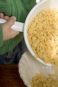 Child tipping wagon wheel pasta out of strainer into bowl