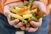 Child's hands holding coloured spiral pasta