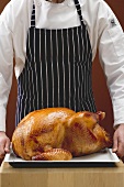 Chef holding stuffed roast turkey on baking tray