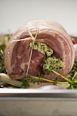 Raw rolled pork joint with herb butter on baking tray