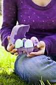 Woman sitting on grass with coloured eggs in egg box