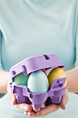 Woman holding egg box full of coloured Easter eggs