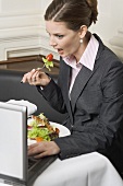 Frau isst Salat bei der Arbeit am Laptop im Restaurant