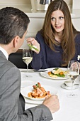 Woman offering man asparagus on fork in restaurant