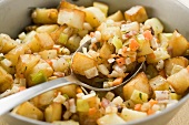 Bratkartoffeln mit Gemüse und Speck in Pfanne mit Löffel