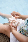 Child holding sea shell on edge of swimming pool