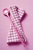 Pink cooking spoon and checked tea towel