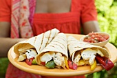 Woman holding plate of wraps and salsa