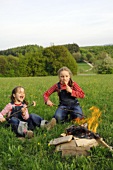 Two girls grilling sausages over a camp-fire