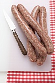 Four sausages on chopping board with knife