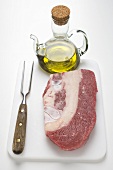 Beef brisket on chopping board, olive oil, meat fork
