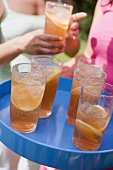 Several glasses of iced tea on tray, women in background